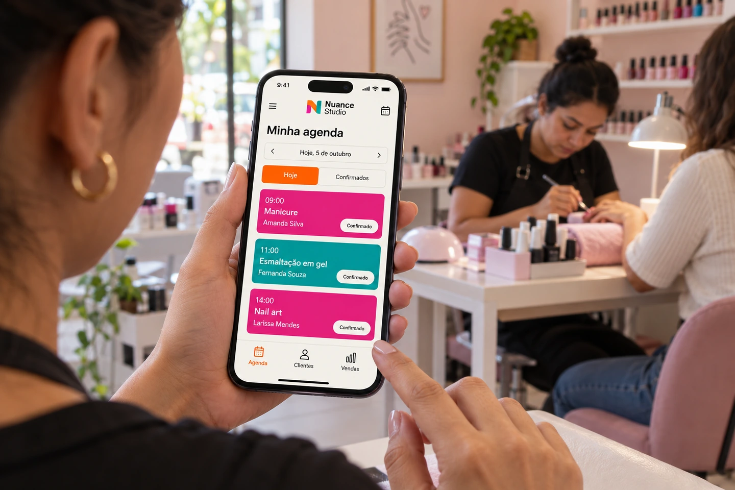 Cena conceitual de um nail studio, com a agenda no celular em primeiro plano e um atendimento ao fundo.